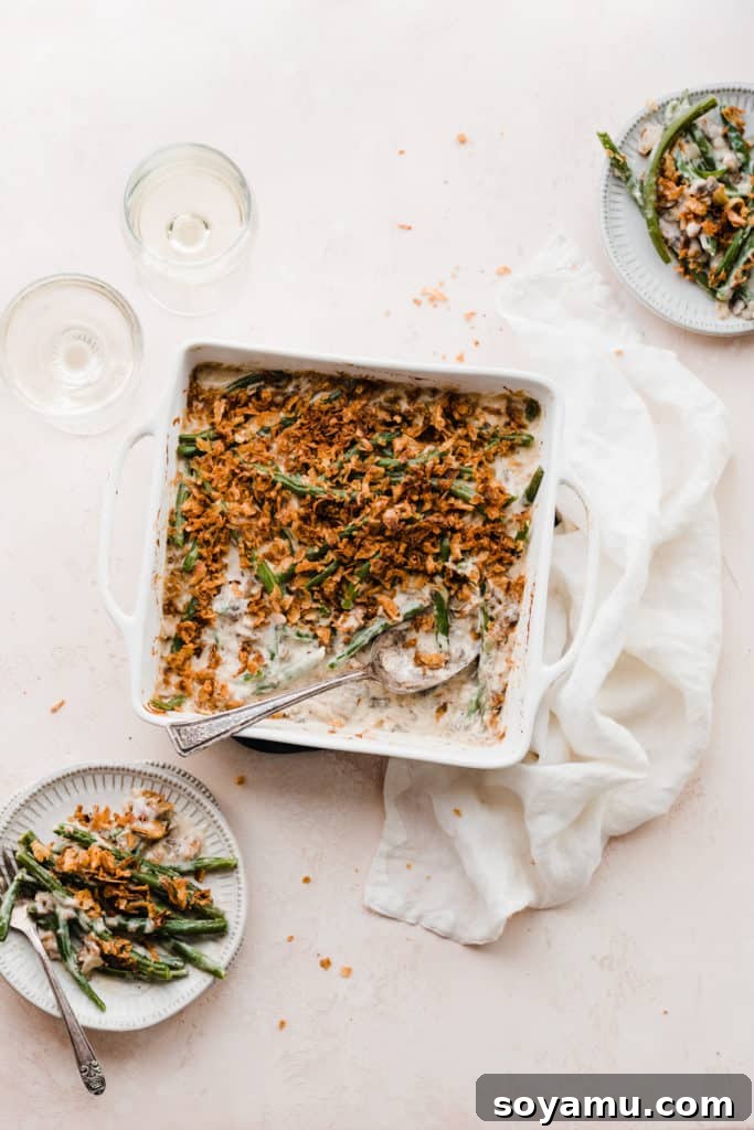 The Ultimate Homemade Green Bean Casserole 2 A beautifully baked dish of homemade green bean casserole, ready to serve, surrounded by festive table settings with a white linen, two wine glasses, and plates of the delicious casserole.