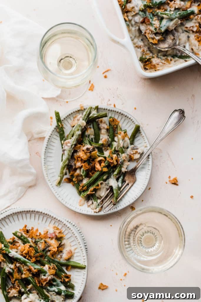 The Ultimate Homemade Green Bean Casserole 10 Two elegantly plated servings of green bean casserole on a festive white linen, accompanied by two glasses of wine, evoking a sense of warm holiday celebration.