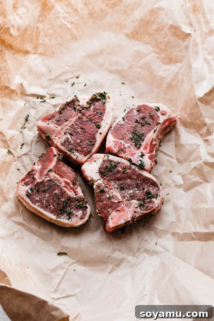 Tender Lamb Chops with Shallot-Thyme Pan Sauce and Creamy Garlic Smashed Potatoes 5 Four uncooked lamb chops, beautifully seasoned with fresh thyme, salt, and pepper, ready for cooking.