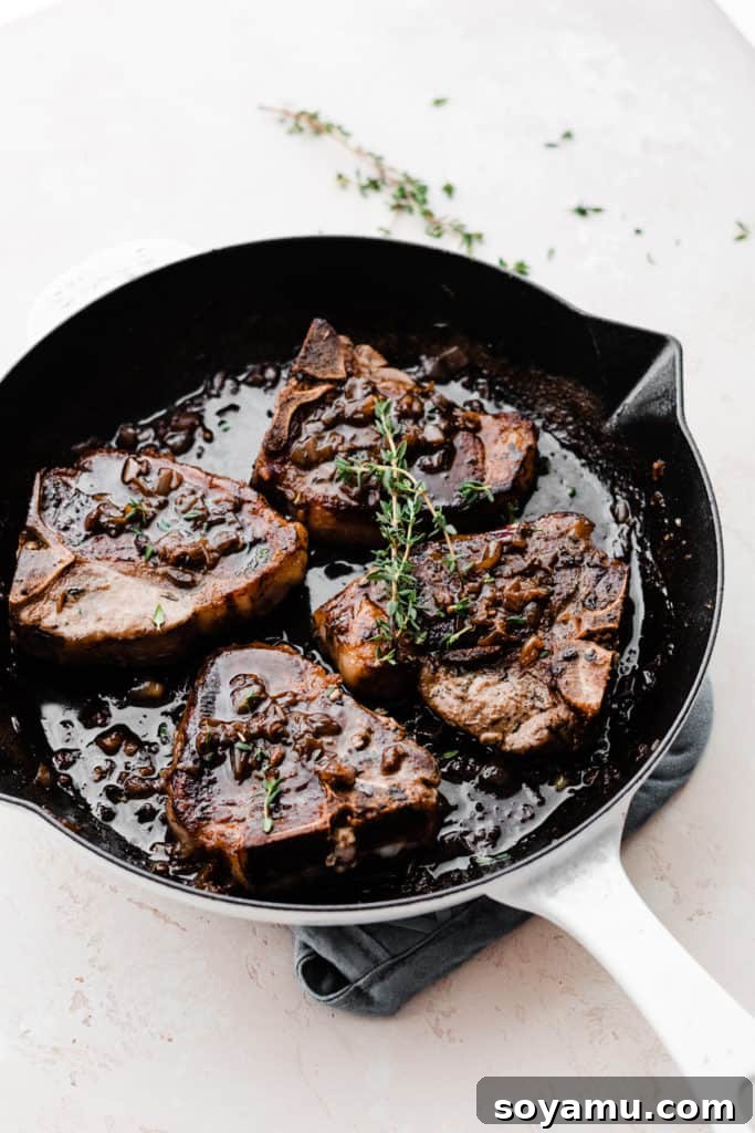 Tender Lamb Chops with Shallot-Thyme Pan Sauce and Creamy Garlic Smashed Potatoes 9 A skillet filled with four perfectly cooked lamb chops, richly coated in the shallot and thyme pan sauce, garnished with fresh thyme sprigs.