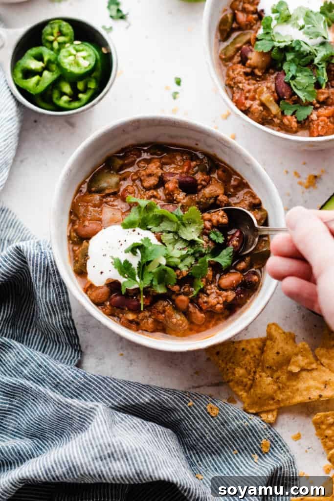 Effortless Slow Cooker Chili Perfection 7 A hand holding a spoon, scooping a generous portion of chunky chili from one of the bowls, highlighting its rich texture and steam.