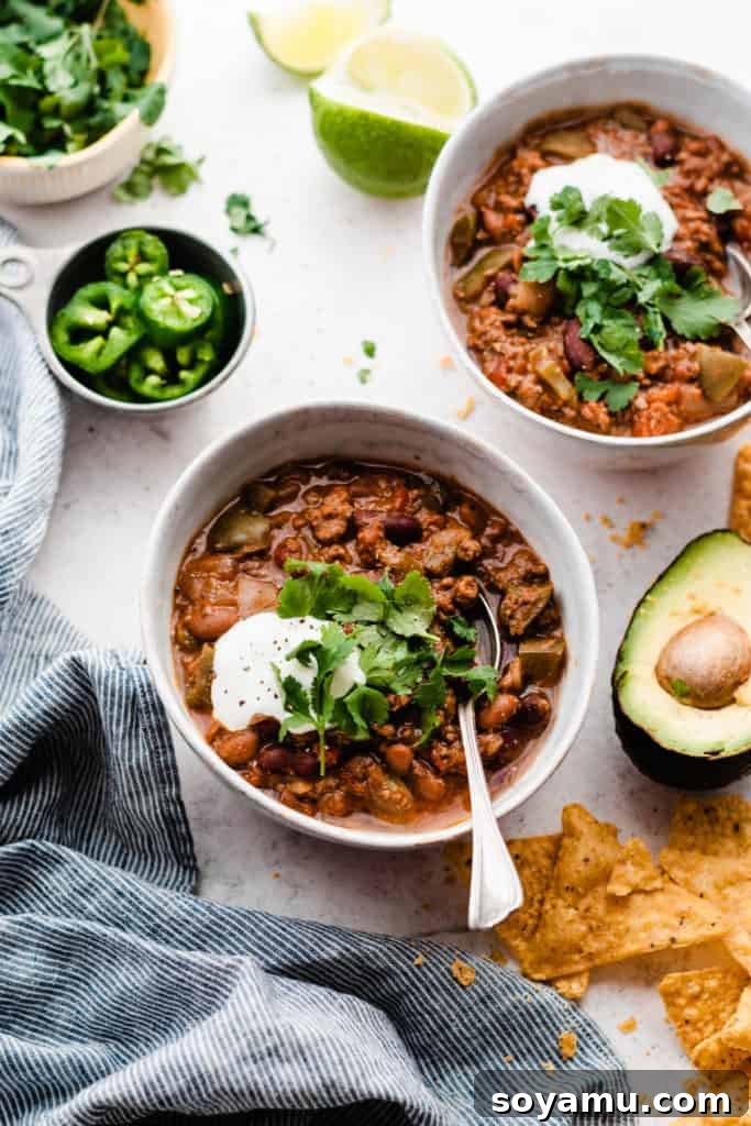 Effortless Slow Cooker Chili Perfection 8 Two aesthetically arranged bowls of slow cooker chili, artfully topped with sour cream and cilantro, surrounded by fresh lime wedges and avocado slices.