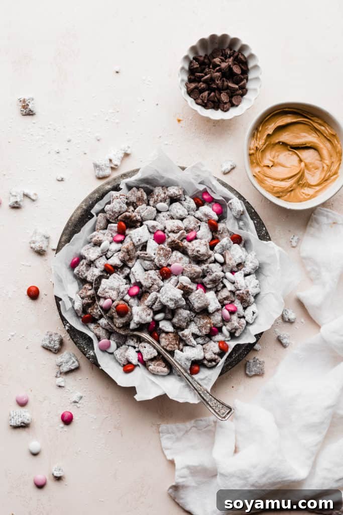 A beautifully presented dish of homemade Muddy Buddies, delightfully adorned with colorful M&M's, artfully arranged alongside separate bowls of rich chocolate chips and creamy peanut butter on a light, inviting surface, ready to be enjoyed or customized.