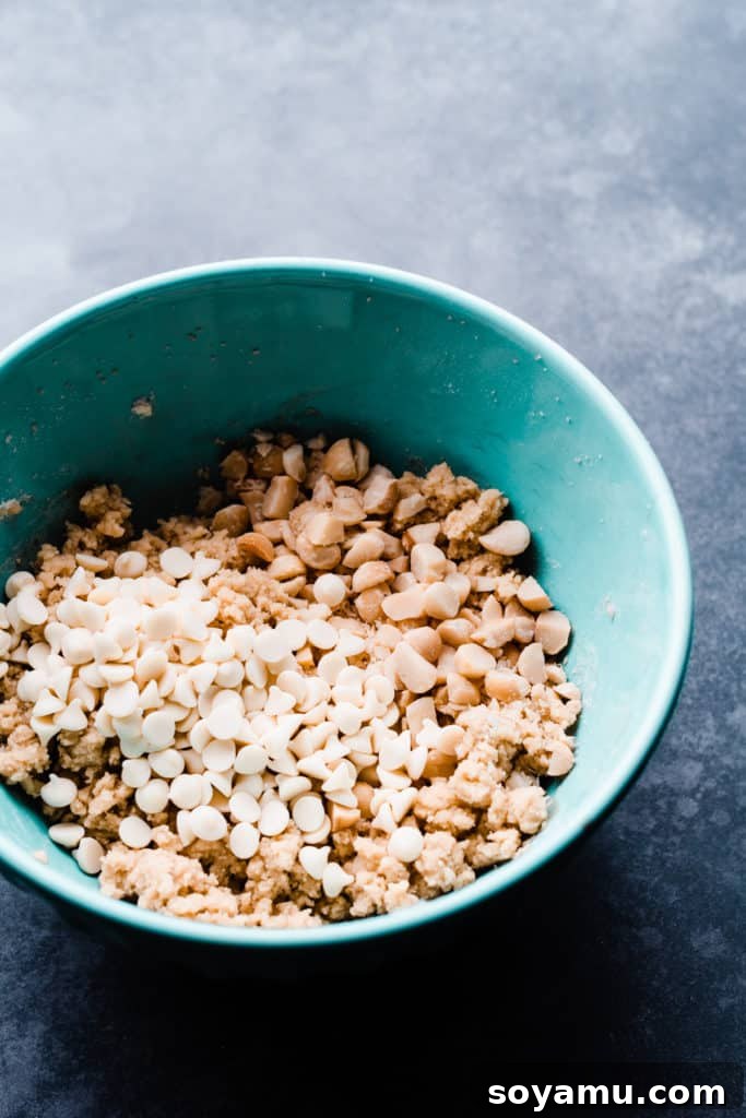 A large mixing bowl filled with rich, creamy white chocolate macadamia nut cookie dough, showing chunks of nuts and white chocolate chips ready for baking.