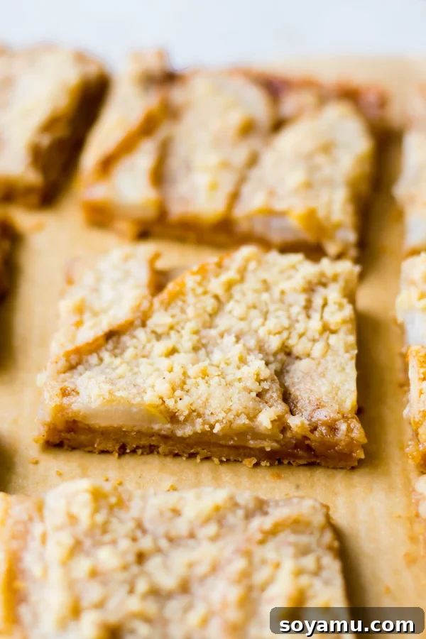 Incredibly Delicious Pear Crumble Bars - A close-up of a pear crumble bar. Close-up shot of a single pear crumble bar, showing the layers of crust, pear, caramel, and crumble.