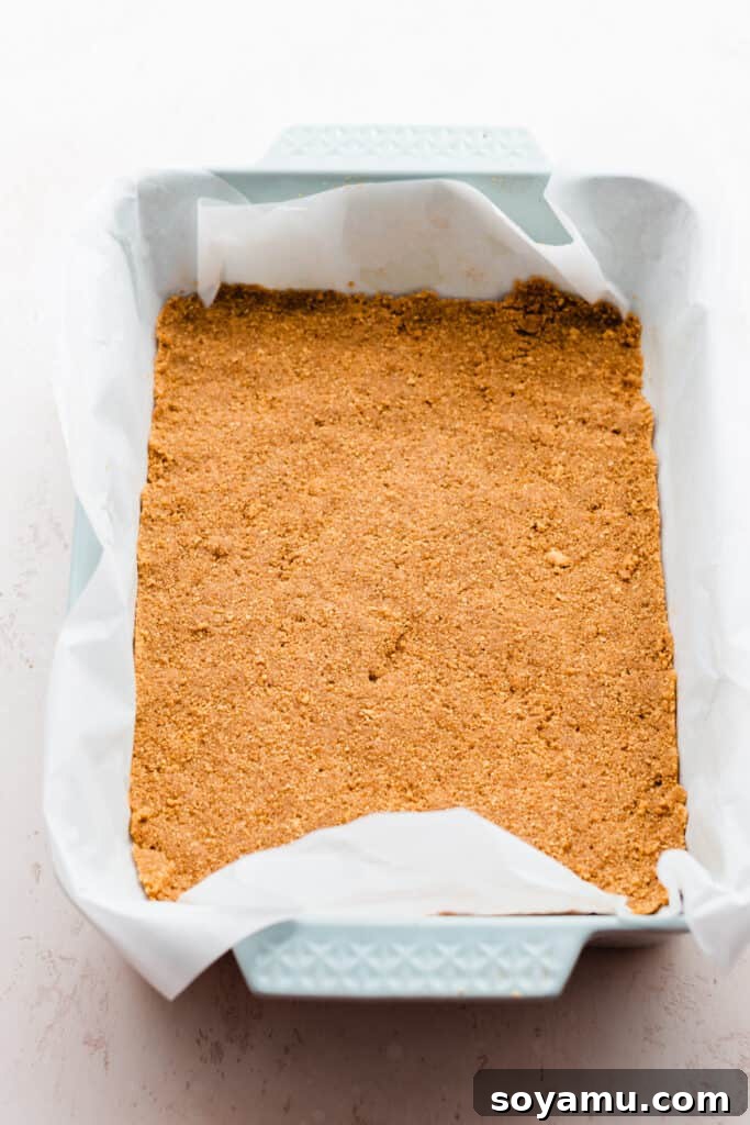 A baking pan meticulously prepared with a golden-brown graham cracker crust, ready for the next layers.