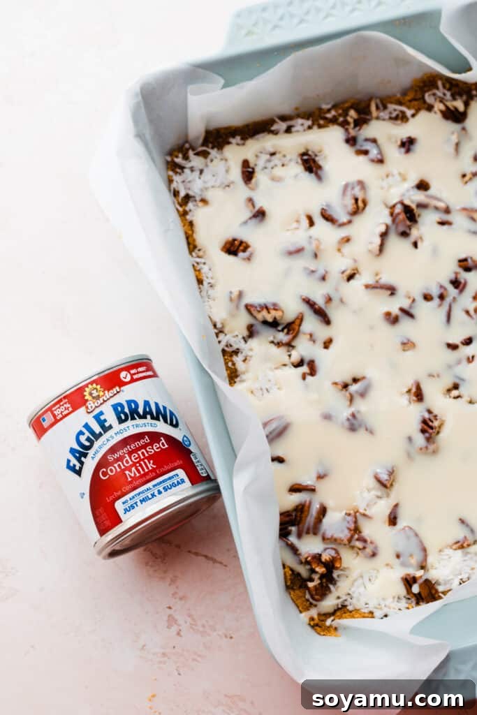 A baking pan showcasing the layers of graham cracker crust, sweet coconut, crunchy pecans, and the rich pour of sweetened condensed milk.