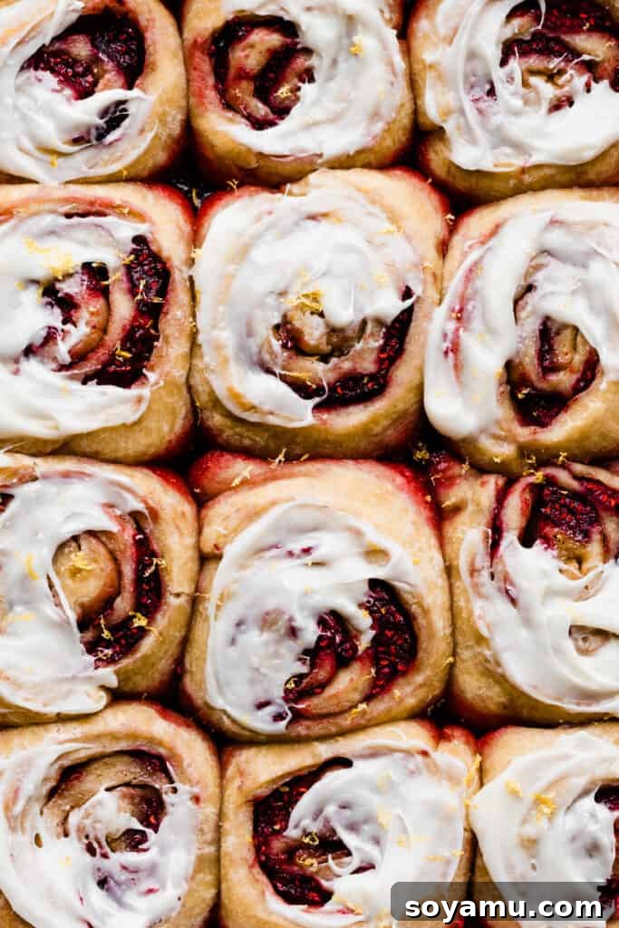 Tangy Raspberry Lemon Morning Buns with Cream Cheese Glaze 2 Sweet rolls iced and topped with fresh lemon zest, ready to be enjoyed.