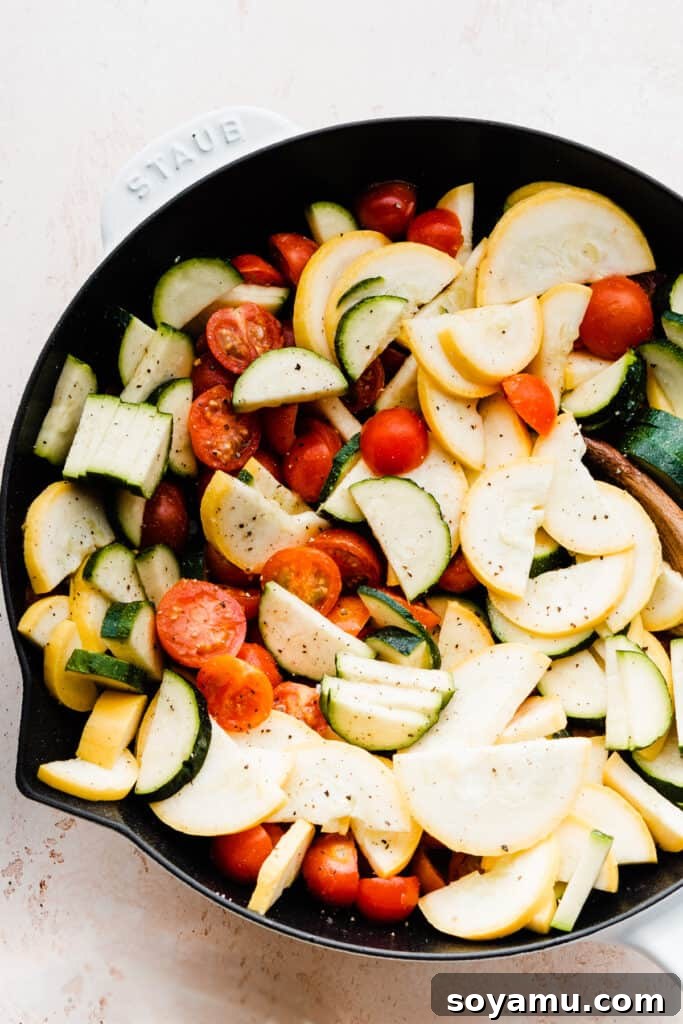 A close-up of a pan filled with uncooked zucchini and cherry tomatoes, ready to be sautéed.