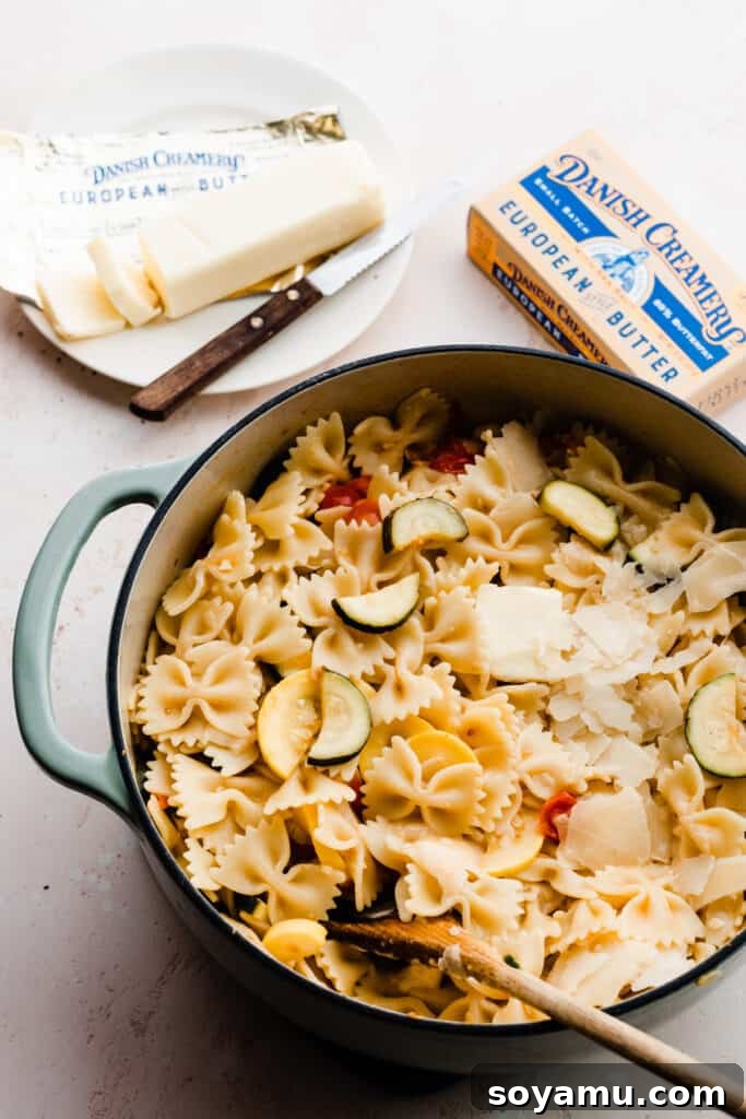 A close-up of rich Danish Creamery butter being stirred into a pot of pasta with vegetables, creating a creamy sauce.