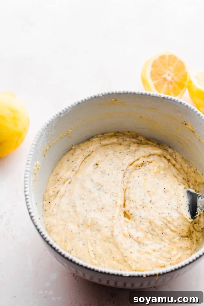 A large mixing bowl containing a light yellow muffin batter, being stirred gently with a white spatula.
