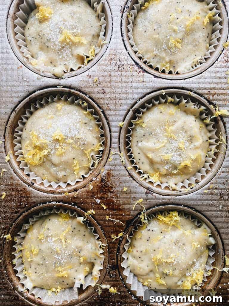 An unbaked pan of muffin batter, each cup generously filled and topped with a sprinkle of granulated sugar and fresh lemon zest.