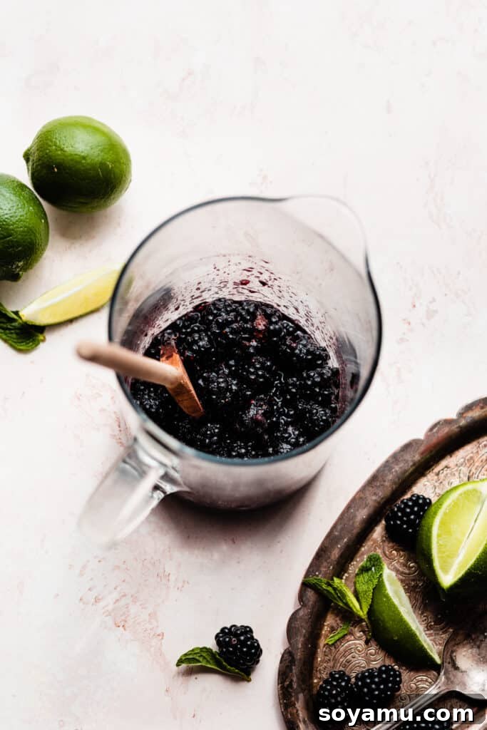 Blackberry Lime Fiesta Sangria 4 A close-up shot of a pitcher containing muddled fresh blackberries and granulated sugar, indicating the first step of the sangria preparation.