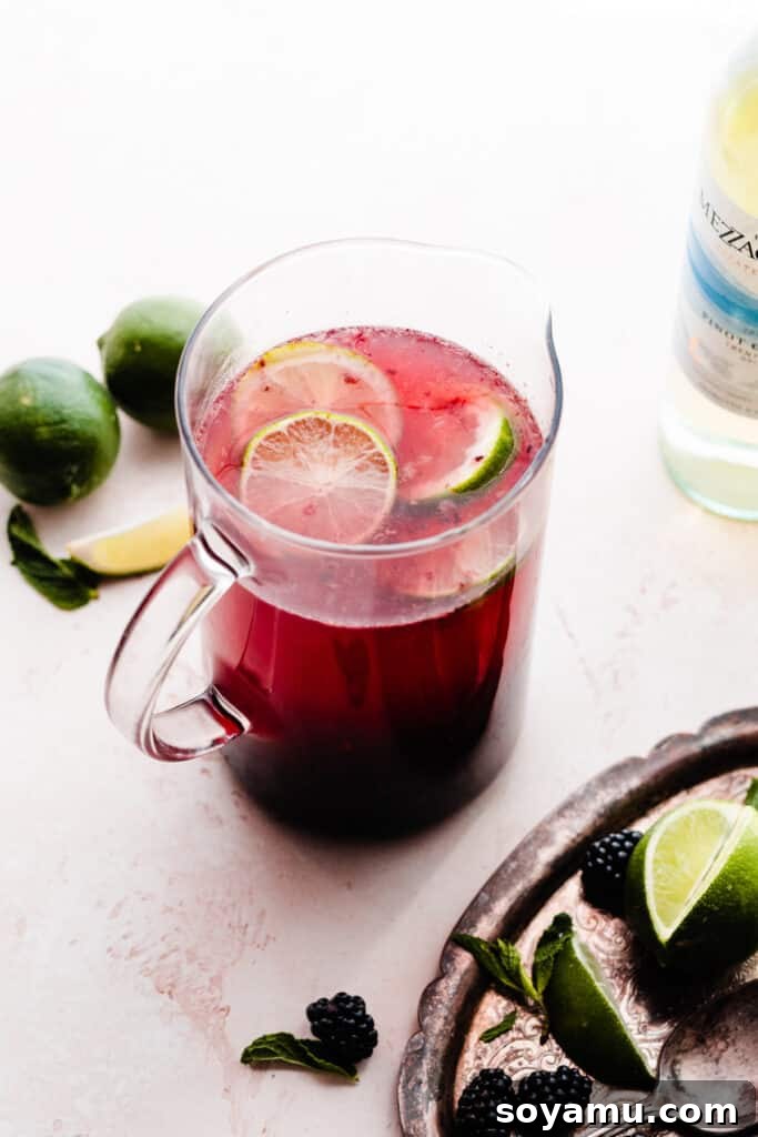 Blackberry Lime Fiesta Sangria 6 A pitcher of the bright pinkish-purple sangria, beautifully topped with fresh lime slices, indicating it's ready for chilling or serving.
