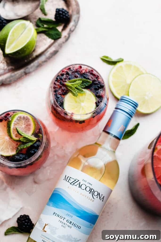 Blackberry Lime Fiesta Sangria 8 An inviting scene featuring two glasses of Blackberry Limeade Sangria, a bottle of Mezzacorona Pinot Grigio, and scattered fresh lime slices, showcasing the key ingredients.