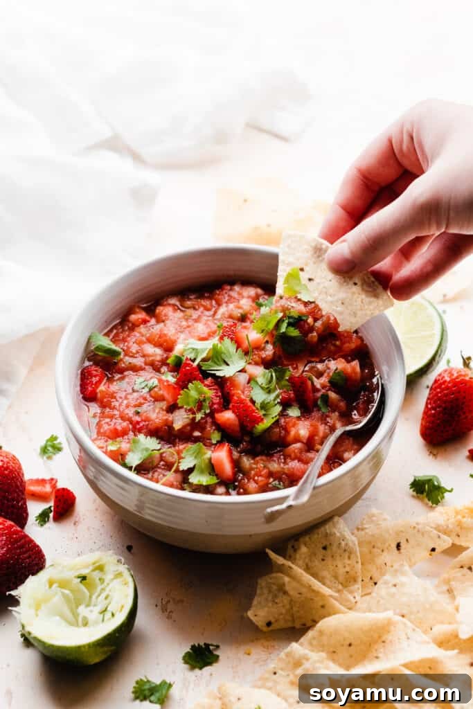 Blended Strawberry Fiesta 2 A crisp tortilla chip being dipped into a bowl of vibrant homemade strawberry salsa, showcasing its chunky texture and fresh ingredients.