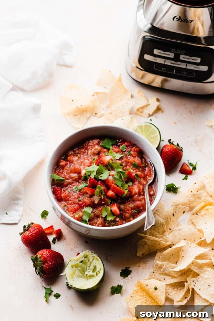 Blended Strawberry Fiesta 3 A colorful bowl of homemade strawberry salsa, garnished with fresh lime slices, whole strawberries, and surrounded by crispy tortilla chips, set against a bright summer backdrop.