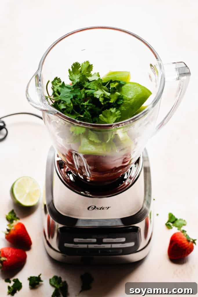 Blended Strawberry Fiesta 5 Fresh cilantro leaves added on top of the chopped vegetables in the blender pitcher, awaiting the next step.