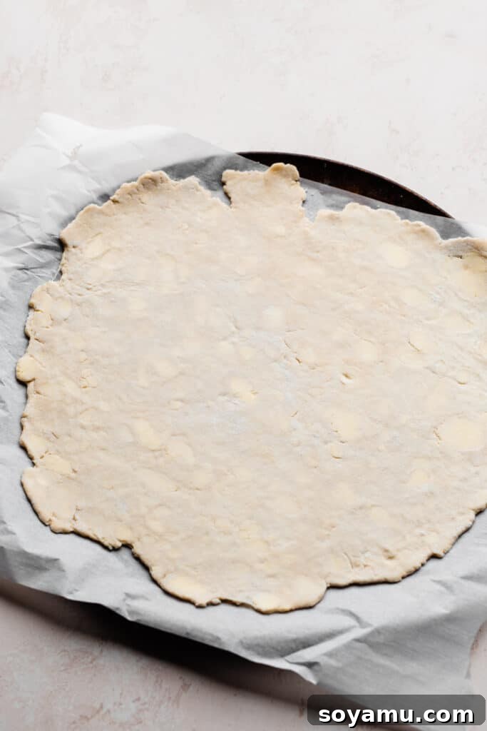 A perfectly rolled out piece of pie dough resting on a parchment-lined baking pan, chilled and ready for the fruit filling.