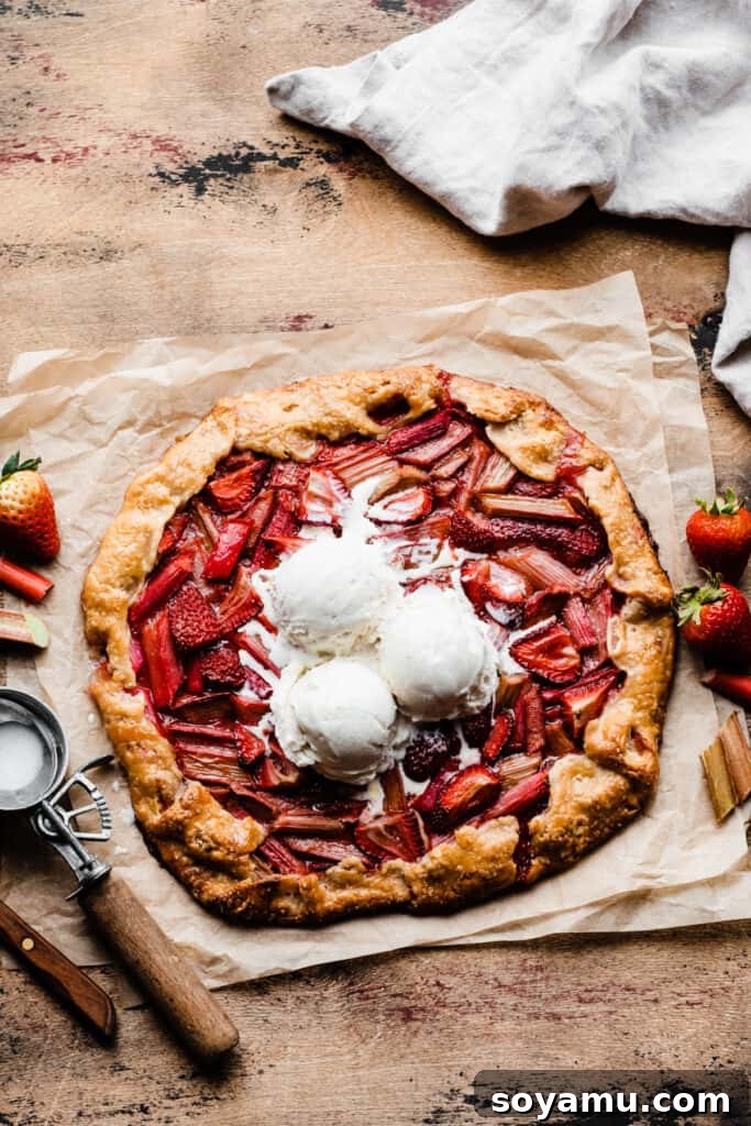 The entire strawberry rhubarb galette, generously topped with multiple scoops of creamy vanilla ice cream, displayed on a warm wooden surface.