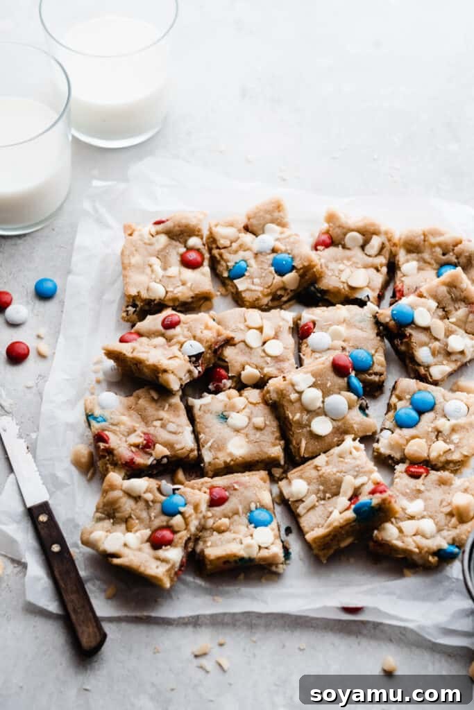 Vibrant M&M Fireworks Cookie Bars 2 The sliced cookie bars on parchment paper with two glasses of milk nearby. A perfect summer dessert.