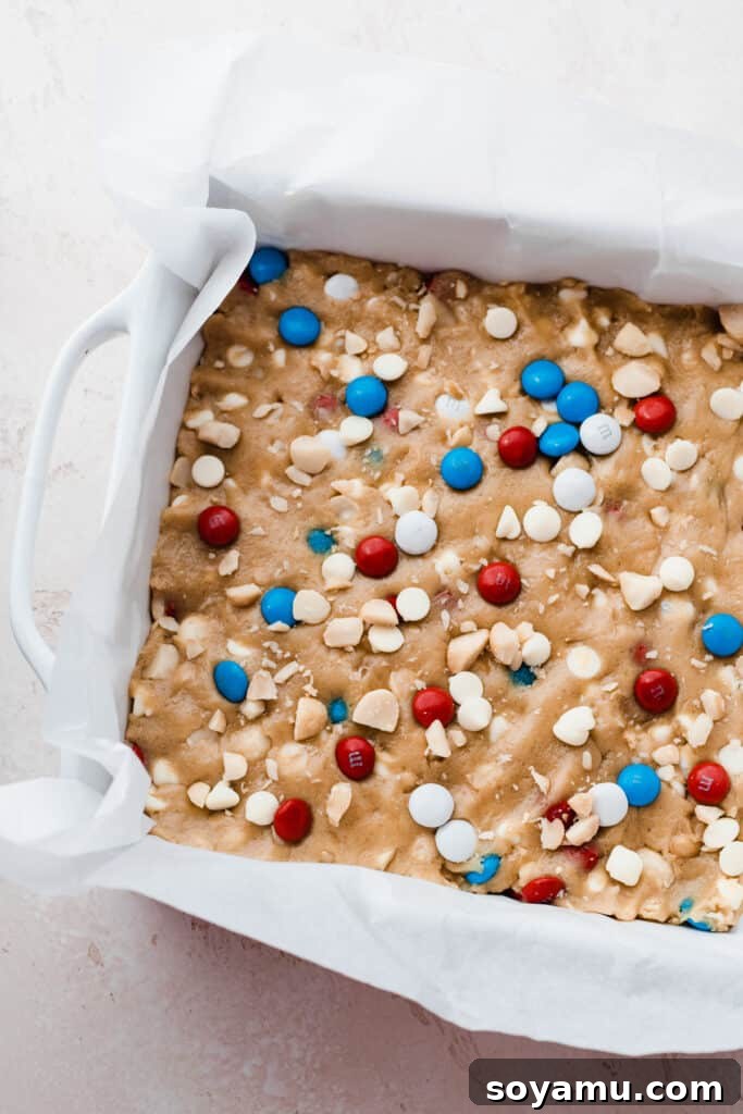 Vibrant M&M Fireworks Cookie Bars 4 A 9x9 pan lined with parchment paper and filled with the cookie dough, awaiting its delicious transformation.