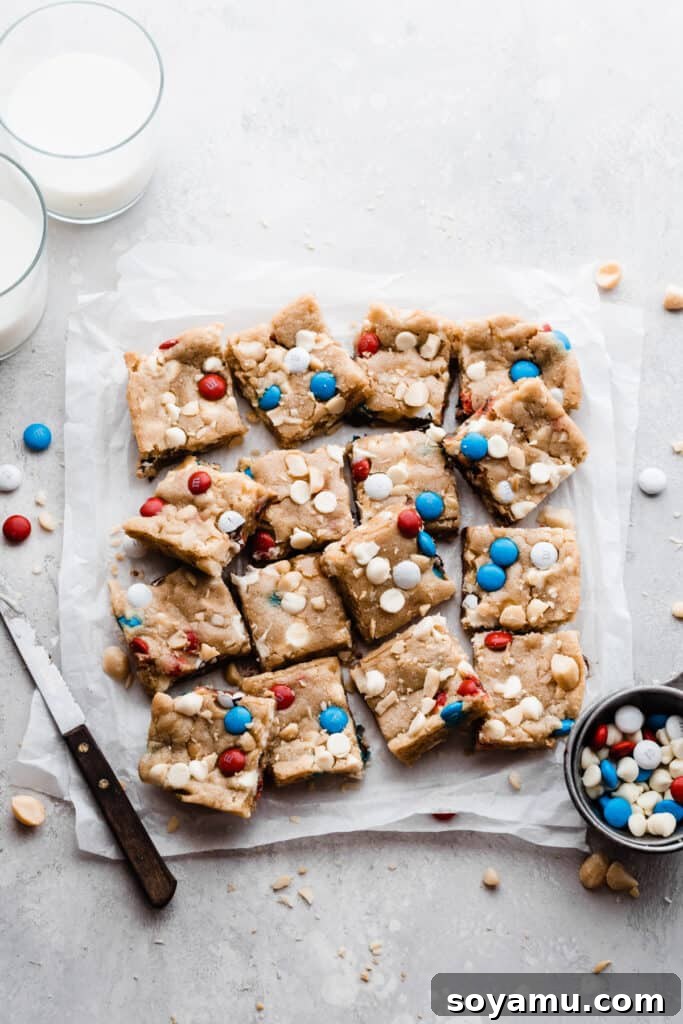 Vibrant M&M Fireworks Cookie Bars 5 The sliced bars on parchment paper, with a bowl of m&m's and two glasses of milk nearby. A delightful display of sweet treats.