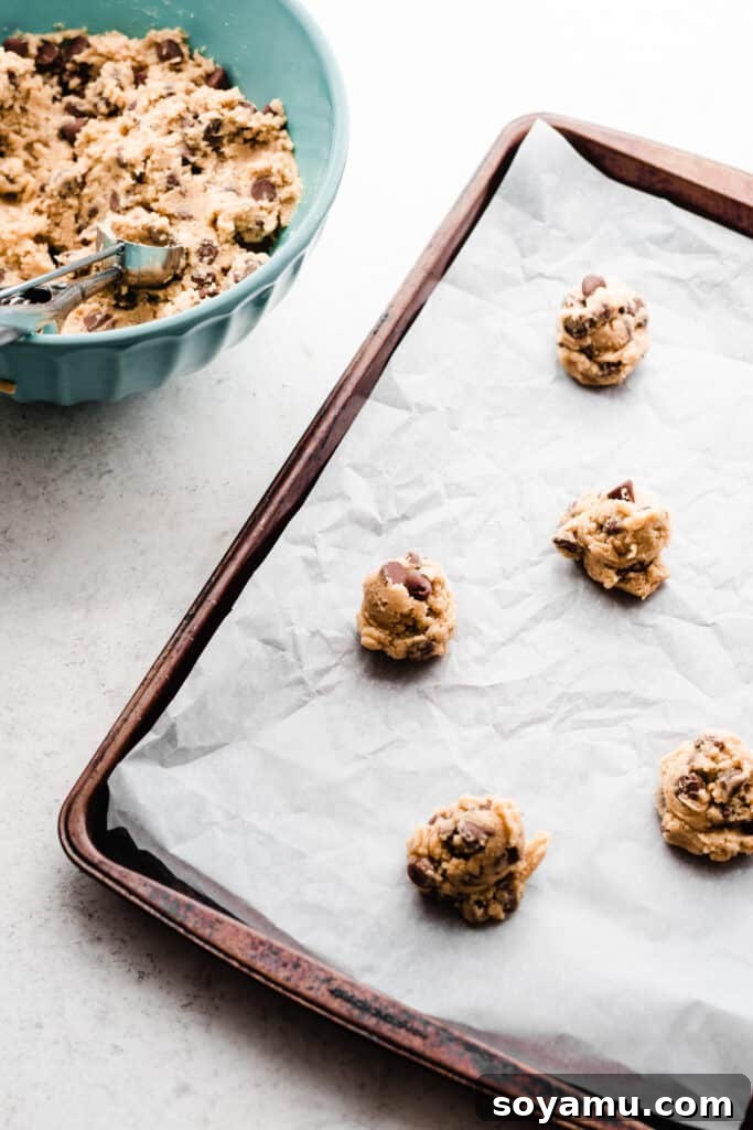 Cookie dough balls neatly spaced on a parchment paper-lined baking sheet, prepared for baking the ultimate soft chocolate chip cookies.