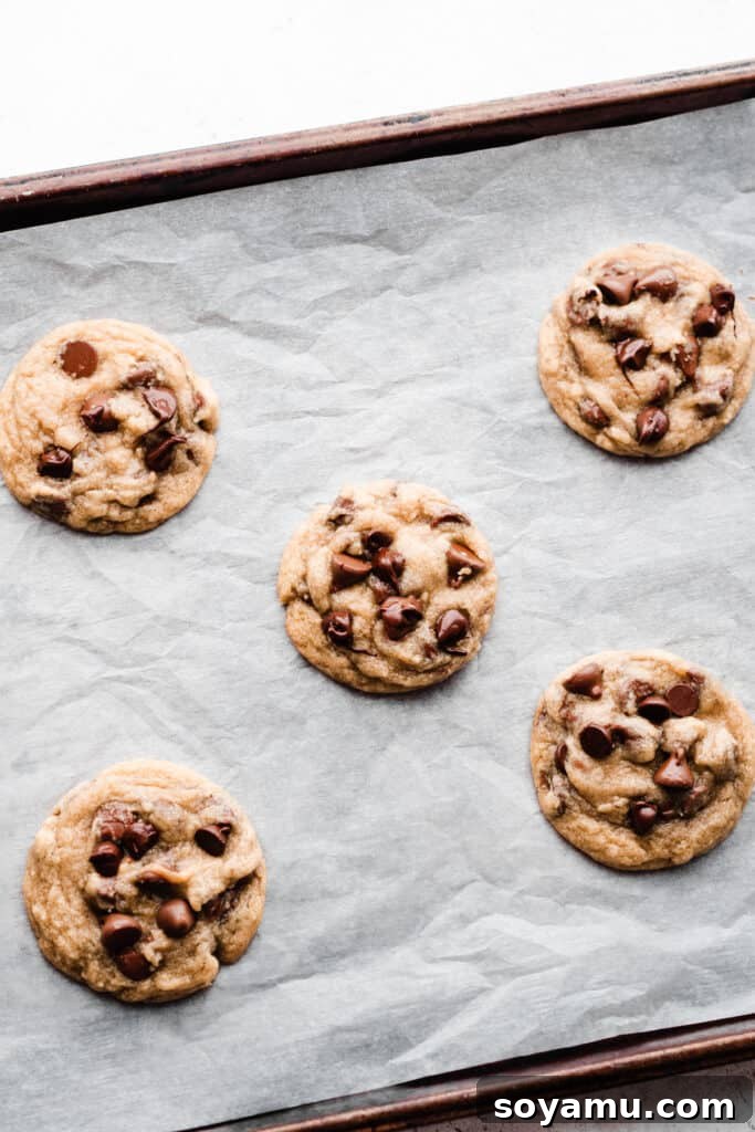 A batch of perfectly baked ultimate chocolate chip cookies cooling on a parchment paper-lined baking sheet, showcasing their golden edges and soft centers.