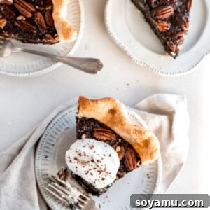 Piece of chocolate bourbon pie topped with whipped cream on a white plate. A bit has been removed from the end of the slice.