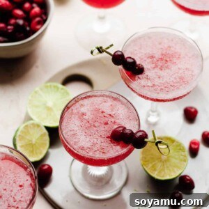 A single glass of frozen cranberry daiquiri, garnished with a lime wedge and cranberries.