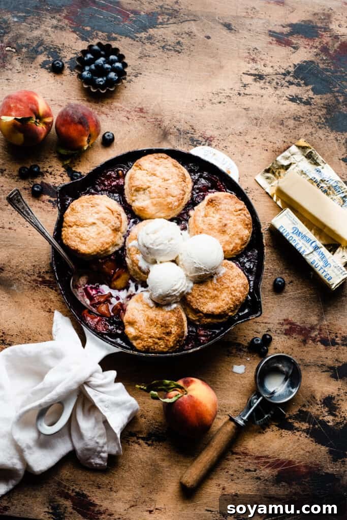 A cast iron skillet filled with golden-topped blueberry peach cobbler, adorned with melting scoops of vanilla ice cream, presented on a rustic wooden surface, capturing the inviting warmth and deliciousness.