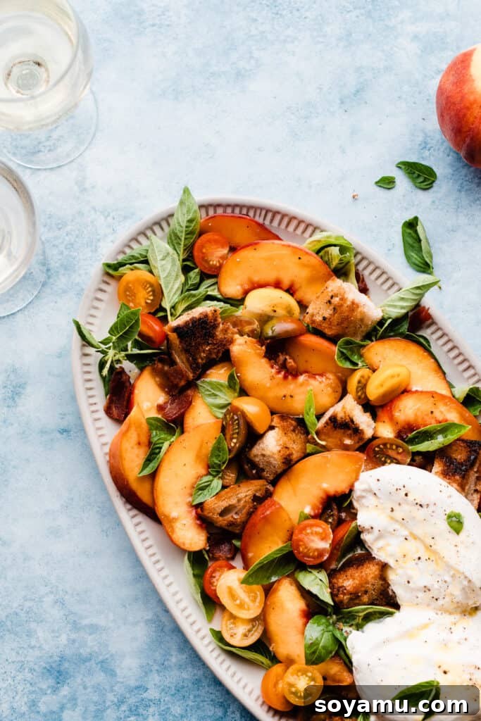 Peach Burrata and Basil Salad 4 A beautifully composed platter of peach burrata salad, featuring a medley of peaches, burrata cheese, crispy bacon, tomatoes, and basil, elegantly presented on a blue surface with wine glasses nearby, suggesting a perfect summer gathering.