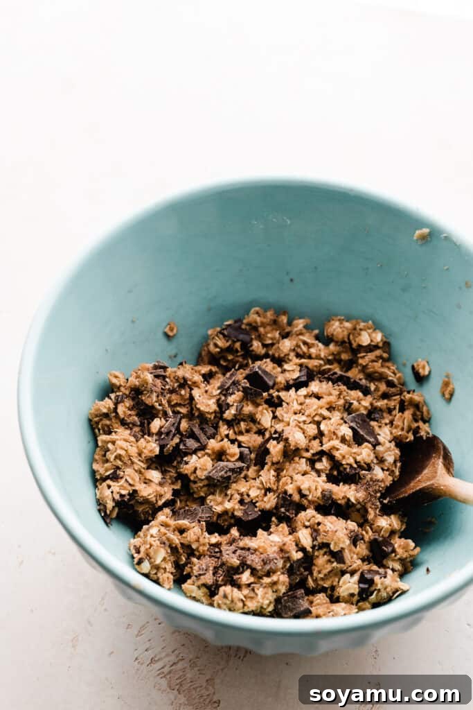 Chewy Brown Butter Chocolate Chunk Oatmeal Bars 5 Rich, thick cookie dough for the oatmeal chocolate chunk bars, studded with large chocolate pieces, resting in a distinctive blue mixing bowl, ready for baking.