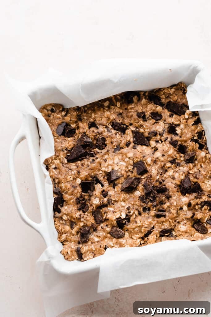 Chewy Brown Butter Chocolate Chunk Oatmeal Bars 6 The unbaked cookie dough for oatmeal chocolate chunk bars, neatly pressed into a parchment-lined 9x9 inch baking pan, ready to go into the oven.