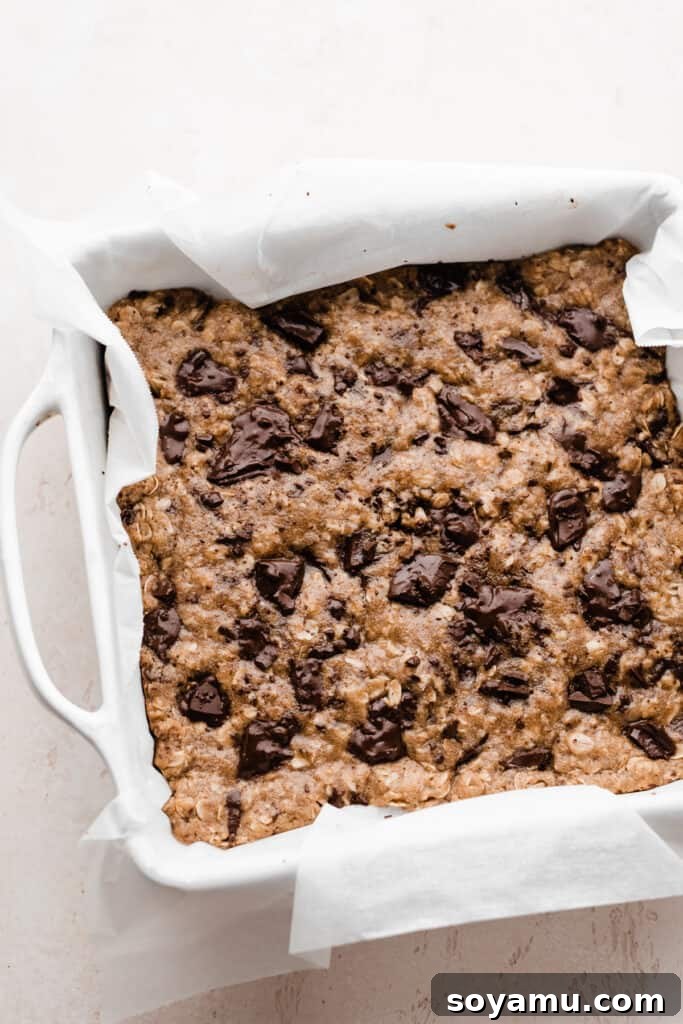 Chewy Brown Butter Chocolate Chunk Oatmeal Bars 7 A pan of freshly baked oatmeal cookie bars, featuring perfectly melted chocolate pools across the golden-brown surface, promising a warm and gooey indulgence.