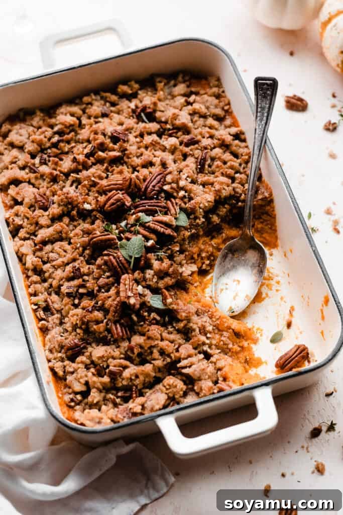 Candied Sweet Potato Casserole with Pecan Streusel 3 A serving spoon rests in the pan of sweet potato casserole, with a few servings already taken.