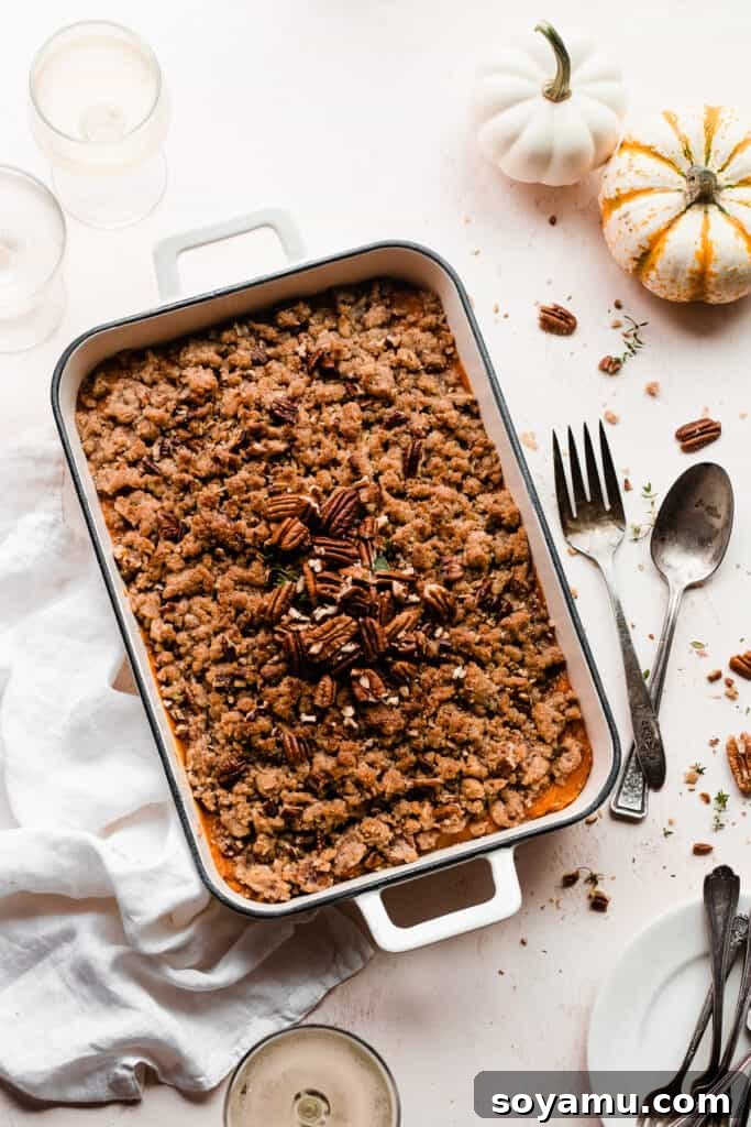 Candied Sweet Potato Casserole with Pecan Streusel 8 The baked sweet potato casserole in a casserole dish, surrounded by serving utensils and wine glasses, ready for a holiday meal.