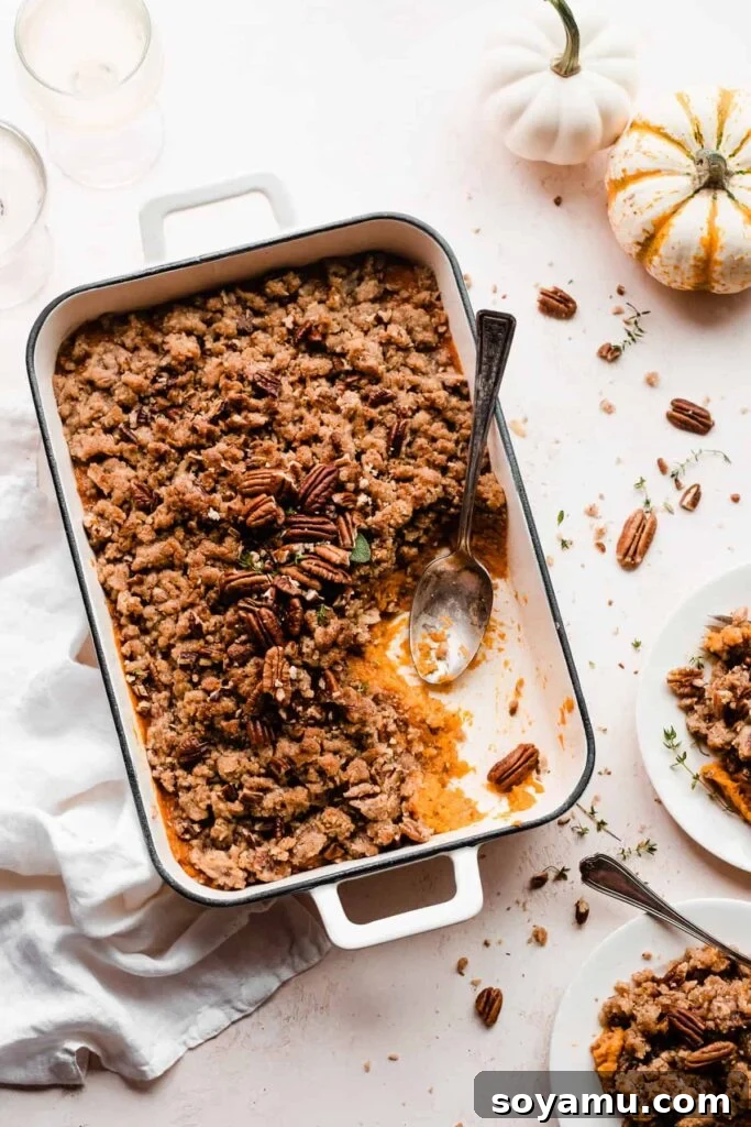 Candied Sweet Potato Casserole with Pecan Streusel 9 A pan of sweet potato casserole being served onto plates with a serving spoon at a festive table.