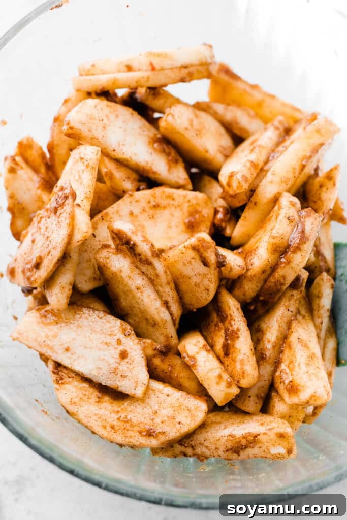 Salted Caramel Apple Galette Recipe 6 A large ceramic bowl filled with freshly sliced apples tossed in brown sugar, flour, and aromatic fall spices, ready for galette assembly.