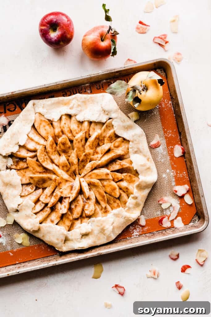Salted Caramel Apple Galette Recipe 7 An unbaked Salted Caramel Apple Galette, carefully assembled with a spiraled apple filling and folded crust edges, resting on a silicone mat-lined baking sheet before baking.