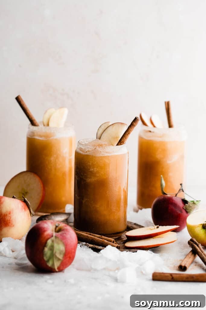 Spiked or Not Apple Cider Slushies 8 Three glasses of apple cider slushies garnished with apple slices and cinnamon sticks, with ice cubes and apples scattered around.