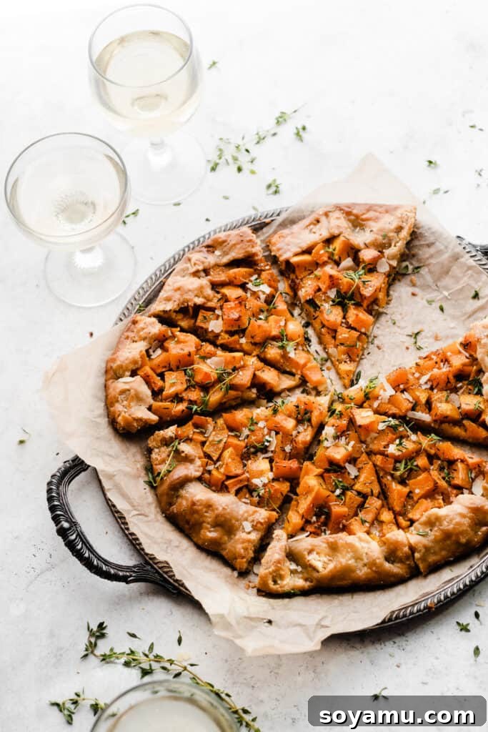 Asiago Parmesan Butternut Squash Galette 2 Sliced butternut squash galette on a vintage metal tray, with wine glasses nearby, showcasing its golden crust and vibrant filling.