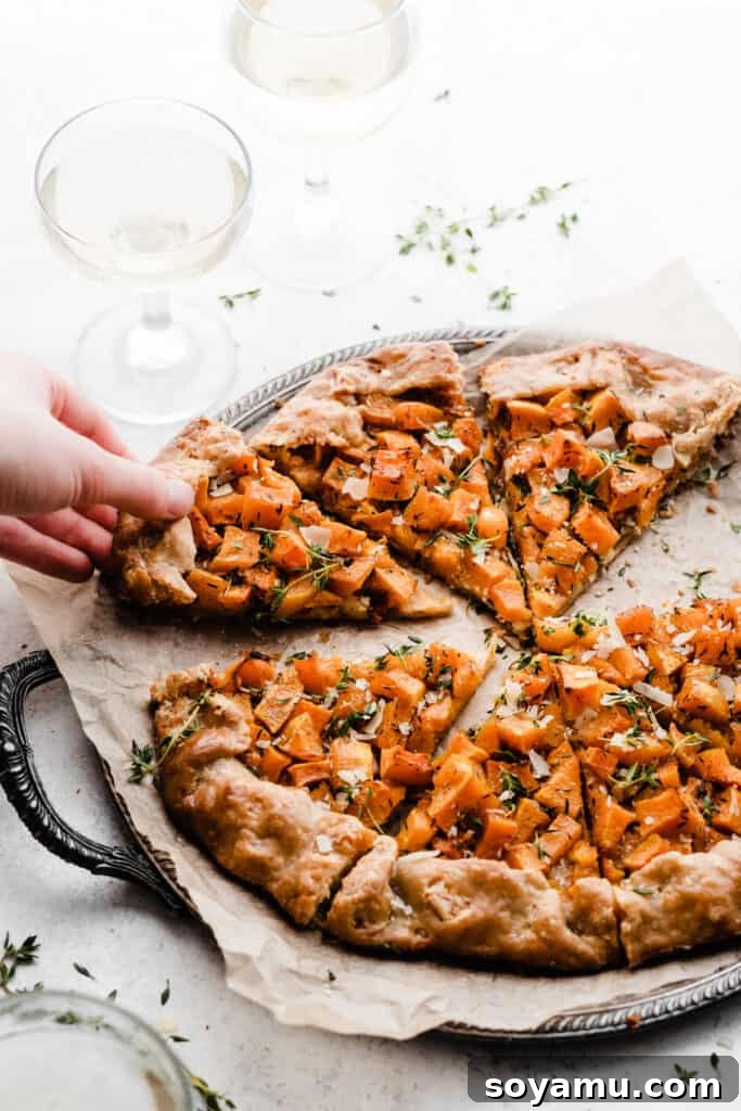 Asiago Parmesan Butternut Squash Galette 8 A hand reaching for a slice of the warm butternut squash galette from the baking sheet, inviting immediate enjoyment.