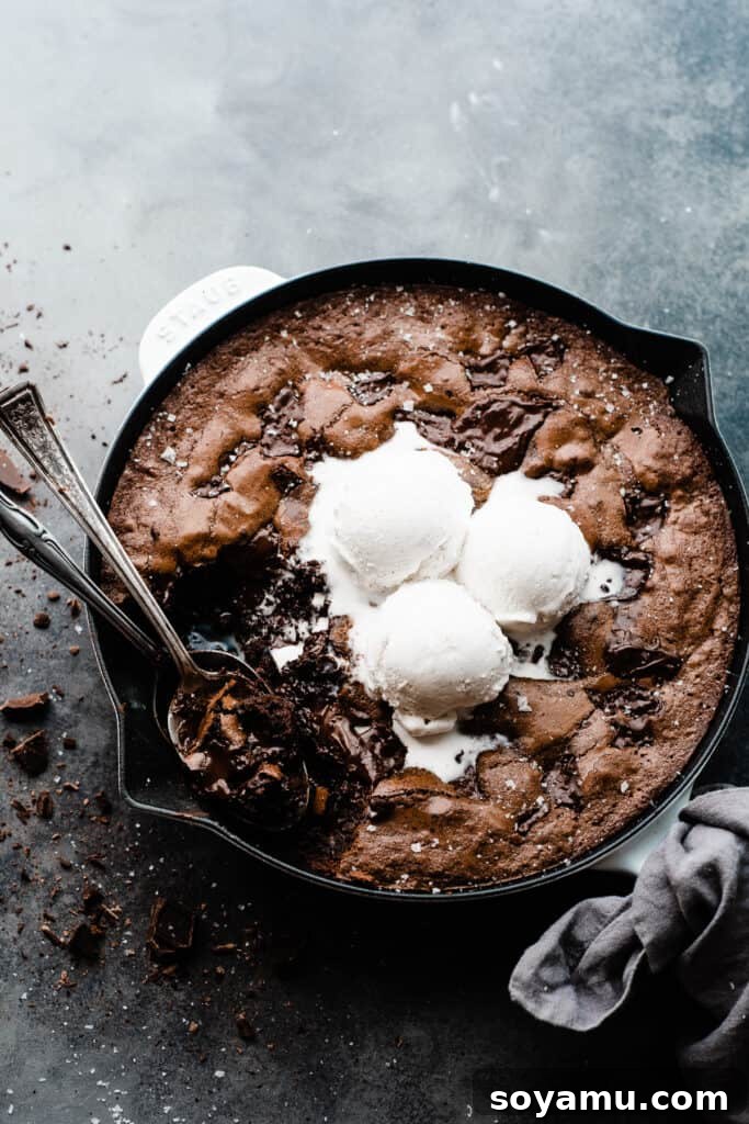 Ultimate Fudgy Triple Chocolate Skillet Brownie 2 A glorious skillet brownie topped generously with vanilla ice cream and two spoons eagerly digging in, highlighting its gooey texture.