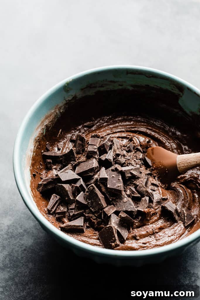 Ultimate Fudgy Triple Chocolate Skillet Brownie 5 A rich brownie batter in a mixing bowl, with chocolate chunks being gently stirred in with a spatula.