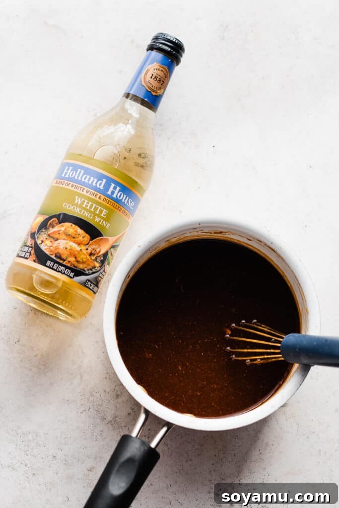 Sticky Sweet Slow Cooker Honey Garlic Chicken 6 A bottle of white cooking wine rests beside a small saucepan of delicious, simmering honey garlic sauce, thickening on the stove for the perfect glaze.
