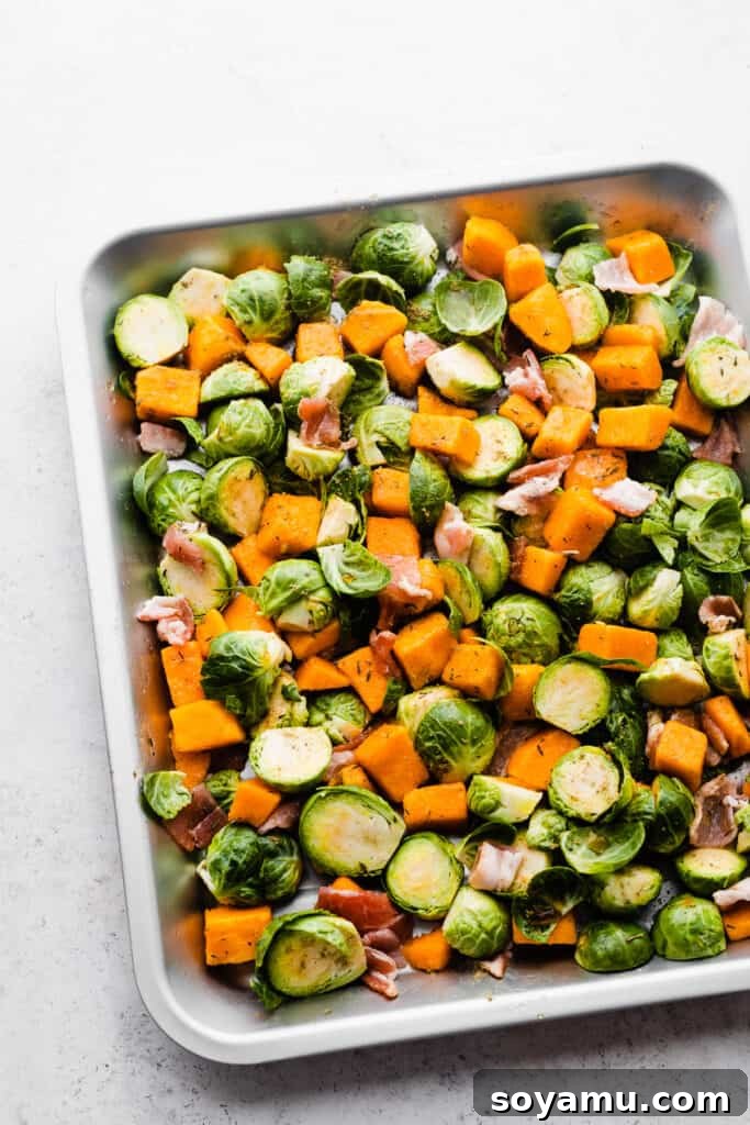 Sweet Maple Roasted Brussels Sprouts and Butternut Squash with Crispy Bacon 3 Raw Brussels sprouts, cubed butternut squash, and slices of uncooked bacon arranged on a baking sheet, ready for seasoning and roasting.