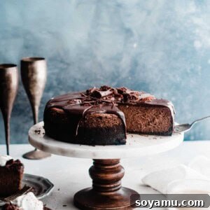 A full Baileys Chocolate Cheesecake on a stand, ready to be sliced, topped with ganache and whipped cream.