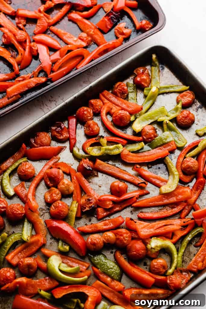 Two baking sheets filled with vibrant red bell peppers, green bell peppers, and cherry tomatoes, beautifully roasted and caramelized, ready for the pasta sauce.